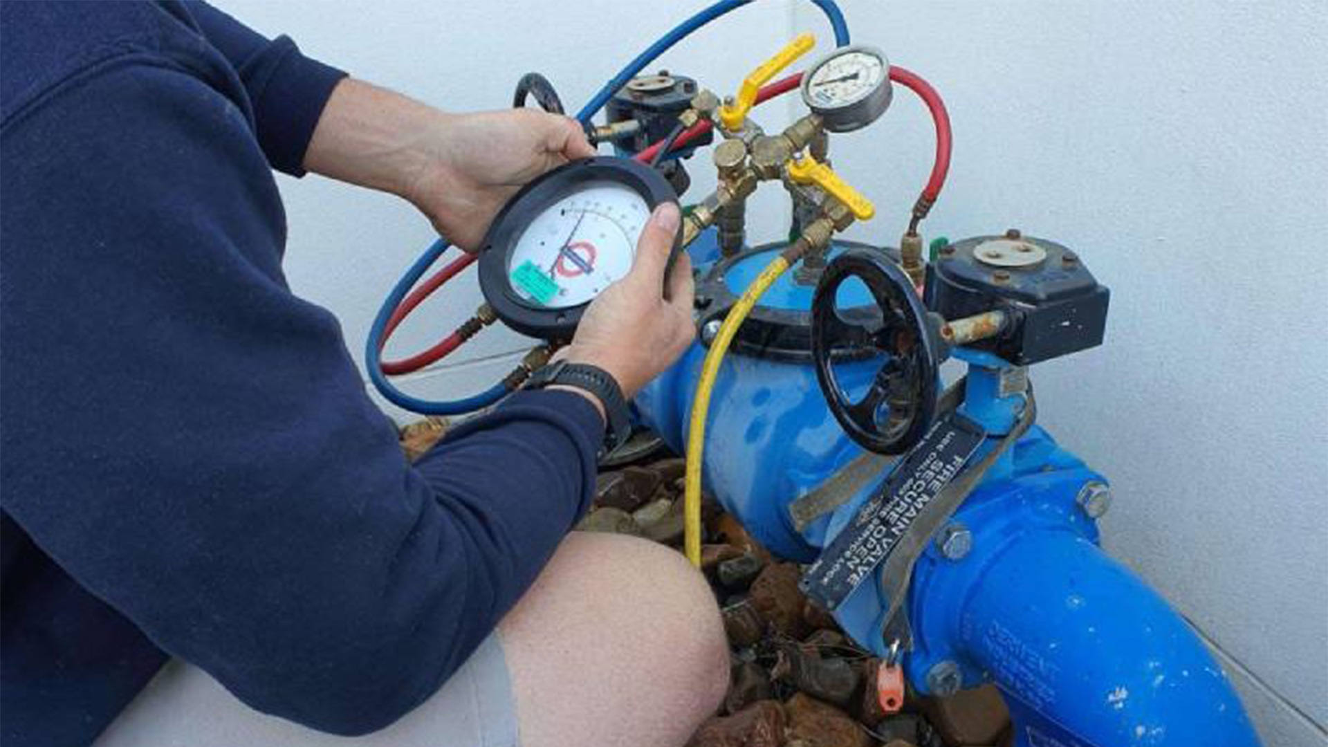 A certified technician performing a backflow test on a prevention device.